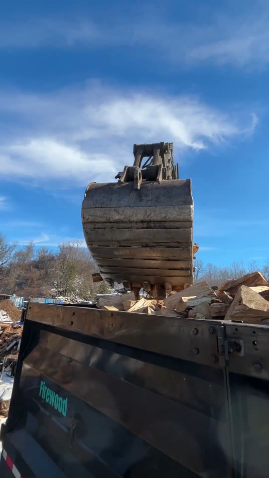 A loader filling a trailer with split firewood