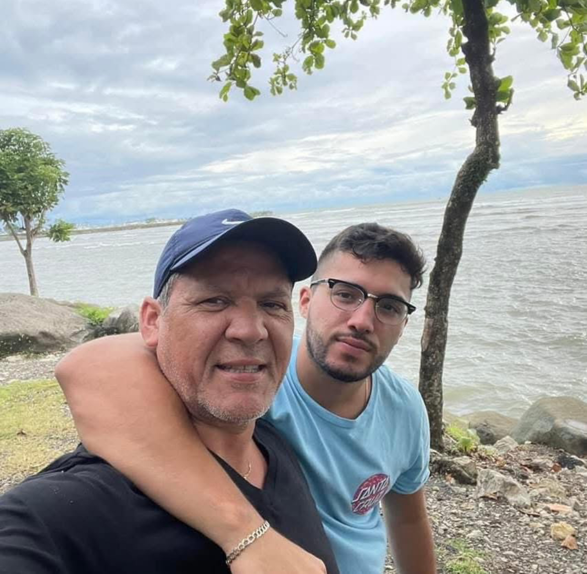 Two people together beside the water, with trees along the shoreline.